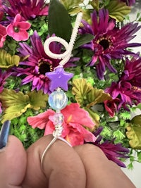 a person is holding a purple star bead in front of flowers