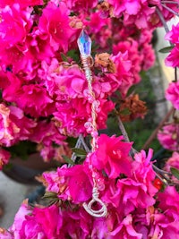 a wand with a crystal in it sits on a pink flower