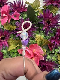 a person is holding a silver bead in front of flowers